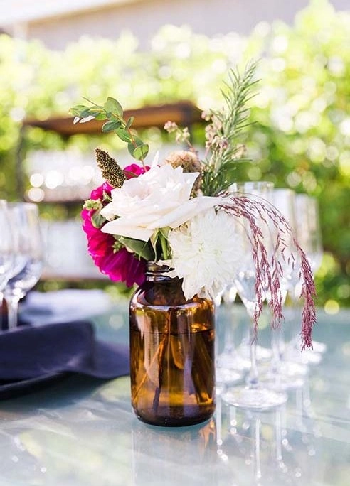 Amber vessel centerpiece with fuchsia, ivory blooms and grasses on a set table