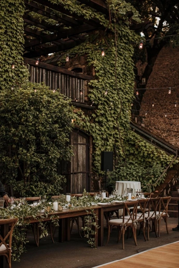 Outdoor long-table dinner with greenery and bistro lights
