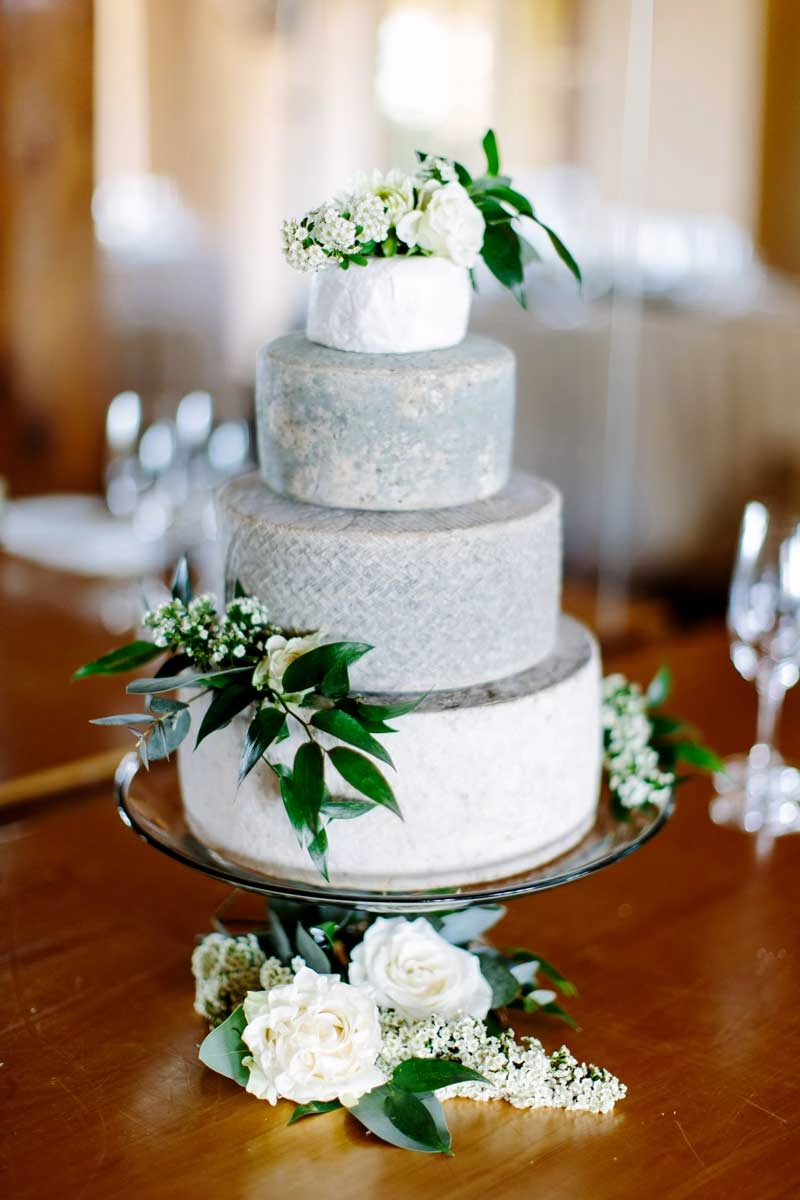 Tiered cheese wheel wedding cake finished with white roses and greenery
