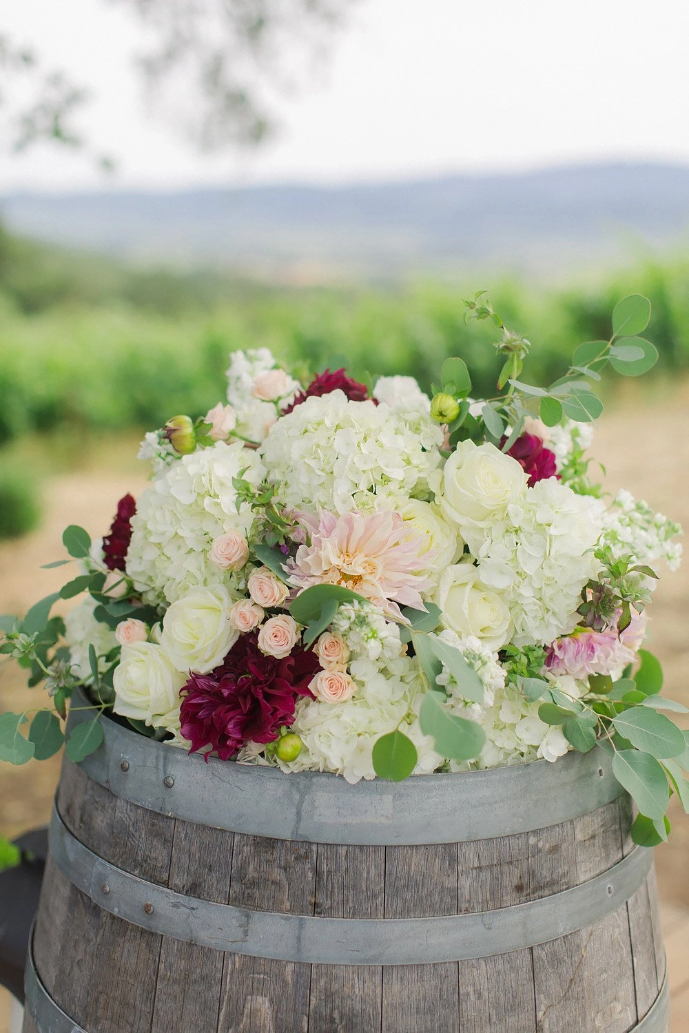 White hydrangea and burgundy dahlia arrangement on a wine barrel