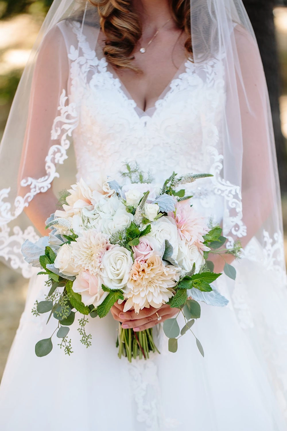 Bride in a lace veil holding a blush dahlia and rose bouquet