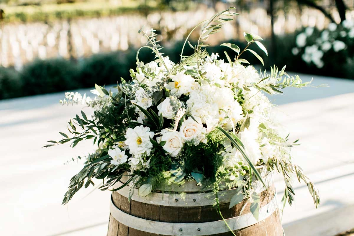 All-white garden arrangement with olive branches atop a wine barrel