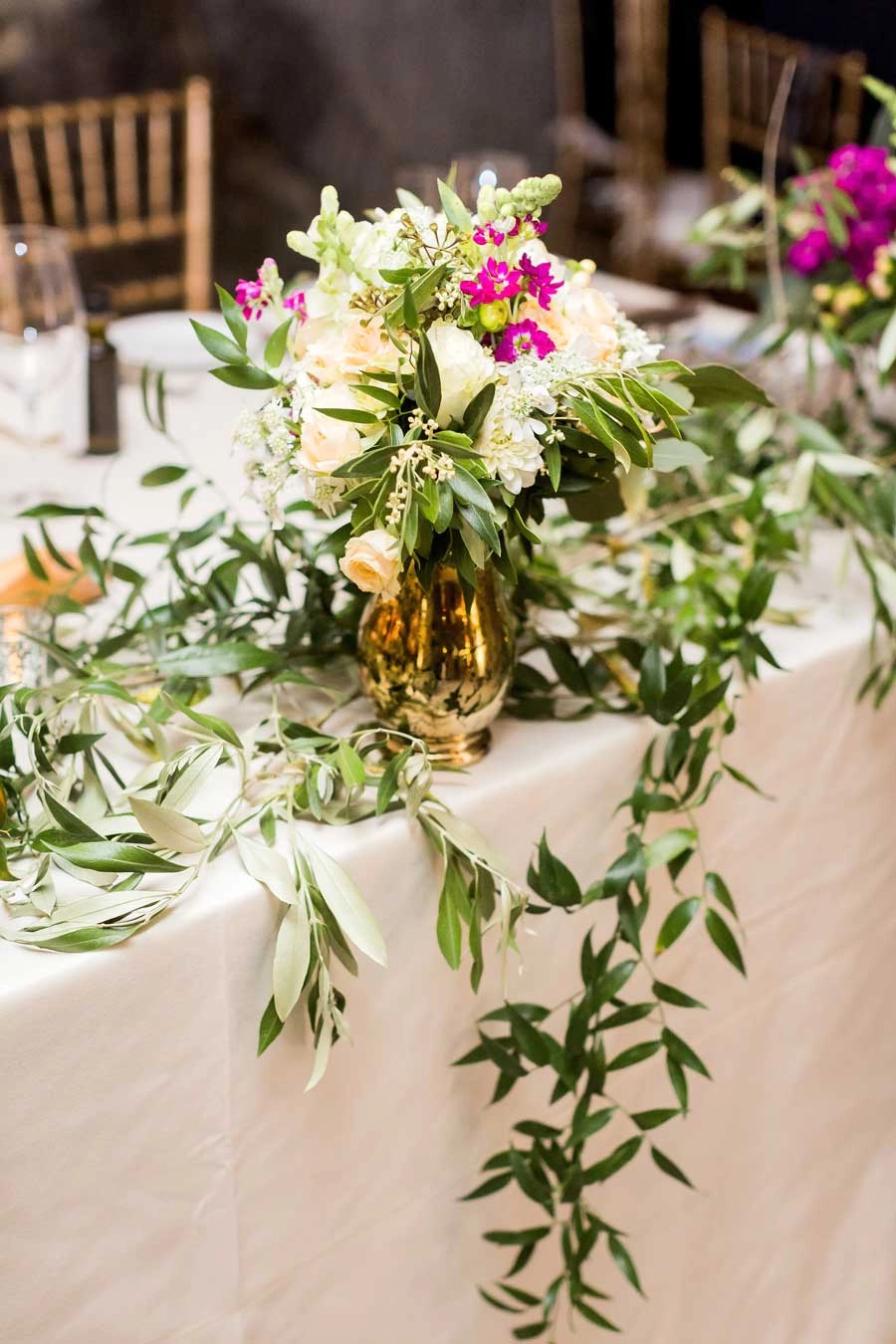 Gold vessel centerpiece with olive garland on a head table